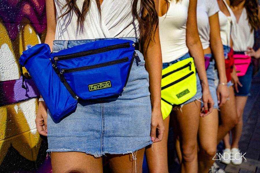 FezPak customizable water-resistant blue fanny pack with detachable bottle holder worn with denim skirt and similar packs in neon colors on models