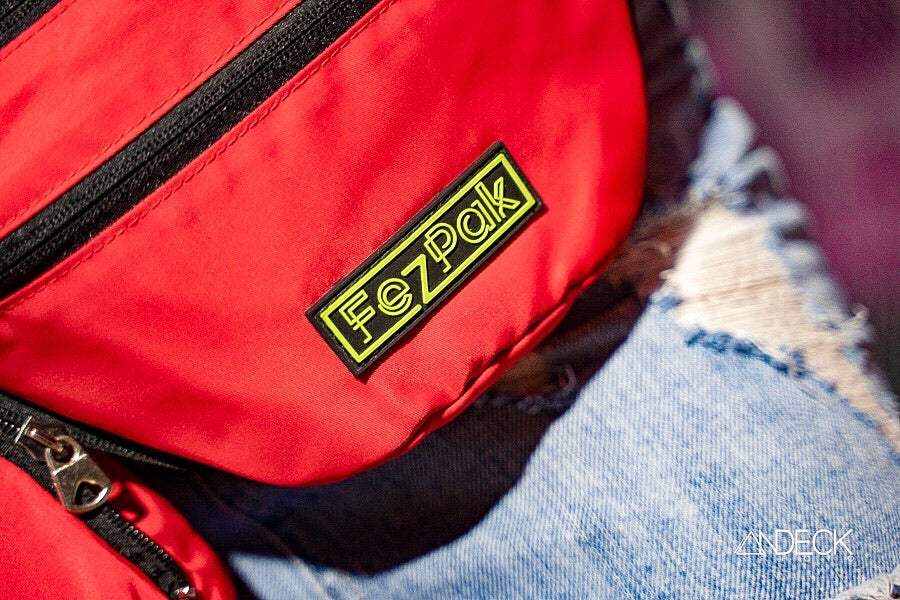 Red FezPak customizable fanny pack with zippered pocket and water-resistant nylon material on denim background