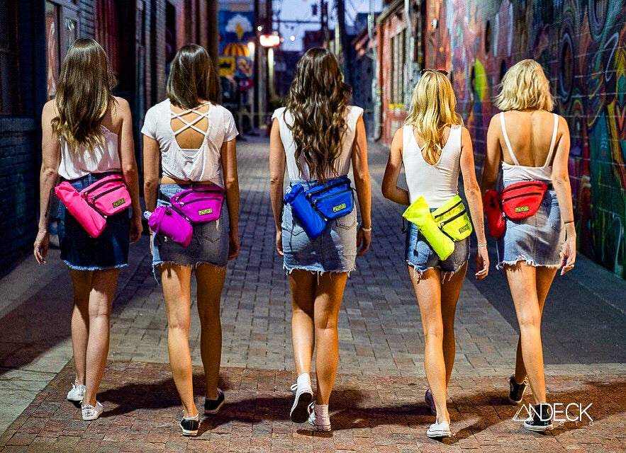 Five women walking in an urban alley wearing colorful FezPak customizable fanny packs and crossbody bags with attachable bottle holders