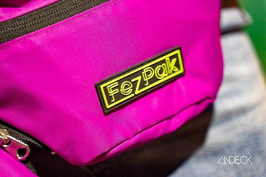 Close-up of bright pink FezPak customizable flat design fanny pack with yellow logo patch and black zipper detailing.