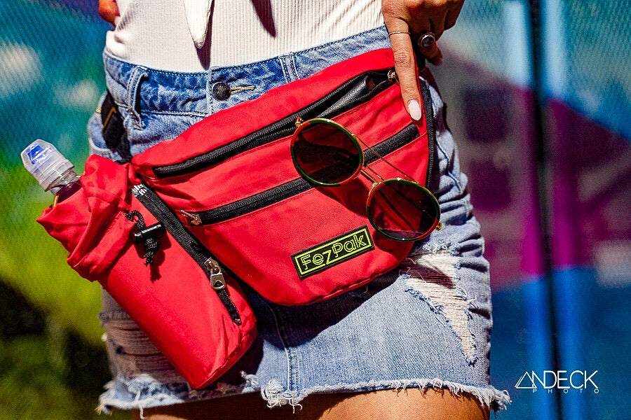 Red FezPak customizable fanny pack with detachable bottle holder and sunglasses attached, worn with denim shorts
