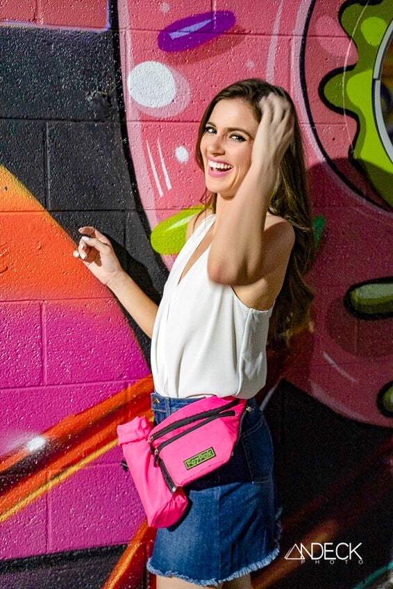 Pink FezPak fanny pack with bottle holder worn by a smiling woman against colorful graffiti background.