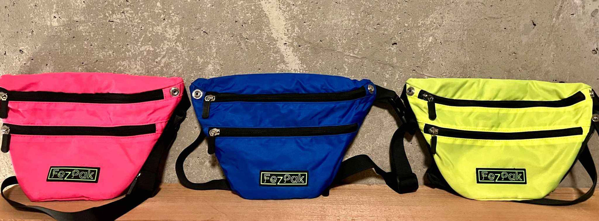 FezPak fanny packs in pink, blue, and yellow with zippered pockets and adjustable straps.