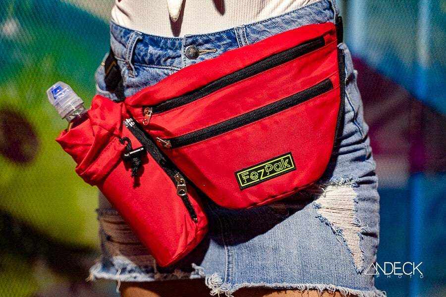 Red FezPak fanny pack with attached bottle holder, worn crossbody over denim shorts.